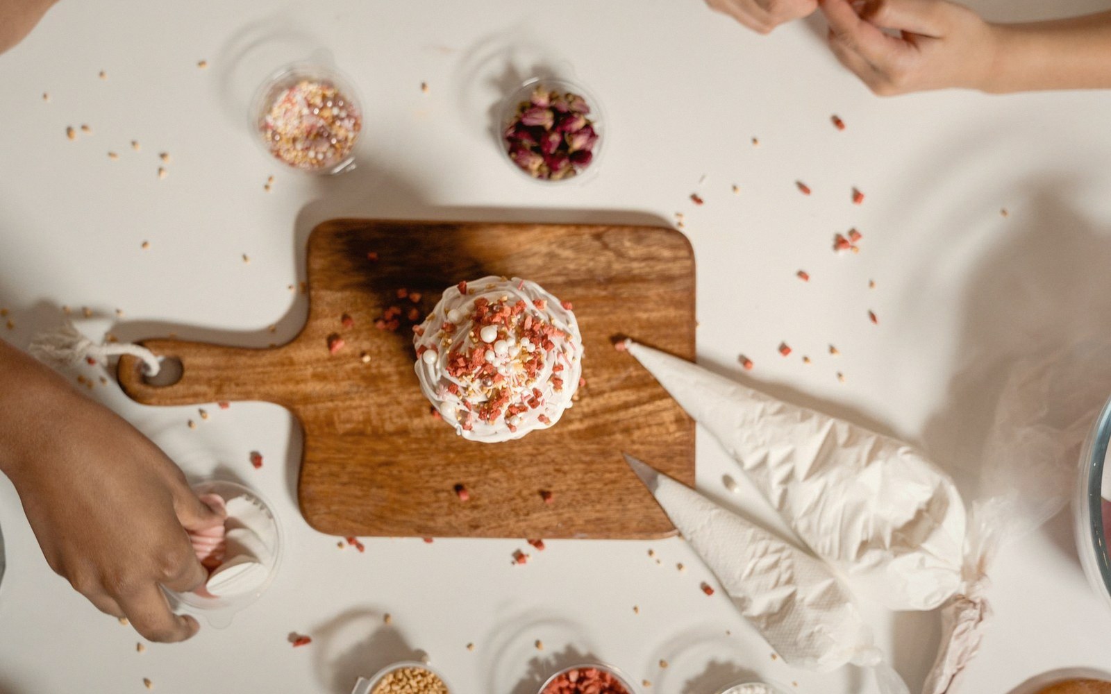 Overhead view of a frosted cupcake on a wooden board surrounded by piping bags and sprinkles
